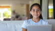 © Ari - Hispanic girl online in living room holding a laptop and earphones