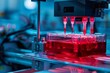 © Tanu - In a modern laboratory, precision equipment dispenses liquid into a clear vessel filled with bright red culture medium, showcasing intricate operations in biological research.