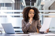 © Tetiana - Serious young African American woman sitting in the office at the desk and thoughtfully looking and studying documents and papers