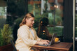 © mdyn - Happy 30s woman doing business on laptop and smiles. Young woman enjoy her work outdoor. Remote work, freelance. Cheerful programmer works remotely on laptop and try to meet deadline outdoor in cafe.