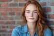 © Milos - A beautiful young woman with auburn hair and freckles poses gently against a rustic brick wall, exuding a captivating and serene smile. The soft lighting enhances her features.