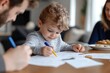 © Milos - A young child is deeply focused on drawing while two adults engage in a creative moment beside them, all set in a bright and inviting home environment.