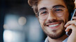 © mahamad - A portrait of a young, cheerful businessman in glasses, smiling and speaking on the phone in his office, representing customer support.