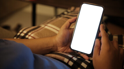 Wall Mural - close up of hands holding a smartphone with a blank white screen, resting in a cozy living room.