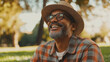 © Papisut - Joyful older man in straw hat enjoying sunny day outdoors, smiling broadly while sitting on grass in a serene park setting with trees and natural scenery