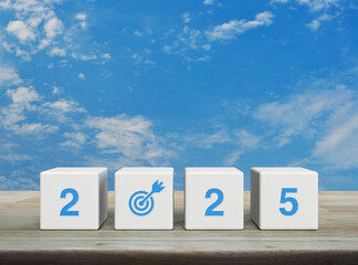 Canvas Print - 2025 letter with goal icon on white block cubes on wooden table over blue sky with white clouds, Happy new year 2025 success concept