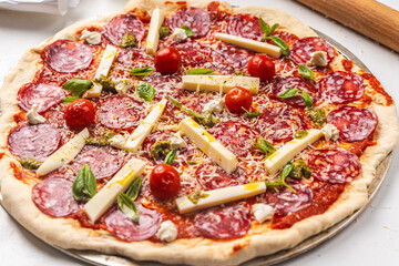 Wall Mural - Pizza is prepared for baking. Raw pepperoni pizza with sausage, mozzarella cheese, cherry tomatoes and basil on a baking wheel