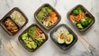 © MRSUTIN - An overhead view of several takeout containers filled with diverse healthy meals, arranged on a light surface.