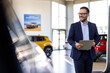 © Graphicroyalty - Successful deal in a car showroom. Handsome male car salesman working in the showroom. Salesperson at car dealership selling vehicles.
