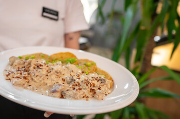 Wall Mural - A close-up of a plate featuring creamy mushroom chicken served with crispy bread. The dish is garnished with green herbs, presented in a cozy dining setting.