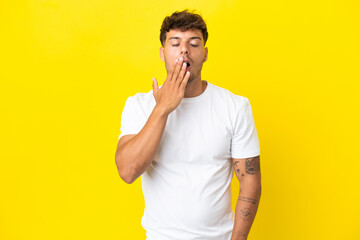 Wall Mural - Young caucasian handsome man isolated on yellow background yawning and covering wide open mouth with hand