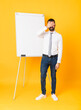 © luismolinero - Full-length shot of businessman giving a presentation on white board over isolated yellow background covering eyes by hands. Do not want to see something