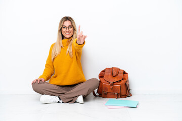 Wall Mural - Uruguayan student woman sitting one the floor isolated on white background showing and lifting a finger