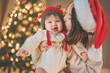 © oatawa - Happy asian mother picks up and kisses baby daughter near Christmas tree at home on Christmas holiday