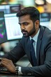 © Andrii Gatchenko - An Indian man financial analyst (35-40) working with graphs on dual monitors wearing a crisp business suit