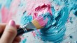 © svastix - A hand holding a brush applies blue and pink paint on a canvas. The artistic act of painting is captured, highlighting creativity and the blending of colors.