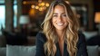 © svastix - A woman with long blonde hair smiling while seated, in a warmly lit indoor space, exuding confidence and warmth, dressed in smart casual attire.