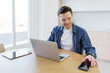 © muse studio - Man working on laptop at bright desk while using smartphone in a modern living space