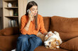 © Home-stock - Young lady worried about her sick Corgi dog calling vet, sitting on couch and touching pet's paw