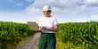© scharfsinn86 - Woman farmer wearing white cap and t-shirt with laptop on agricultural field