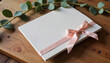 © Irina - Elegant blank notebook tied with a soft pink ribbon, adorned with greenery on a rustic wooden surface