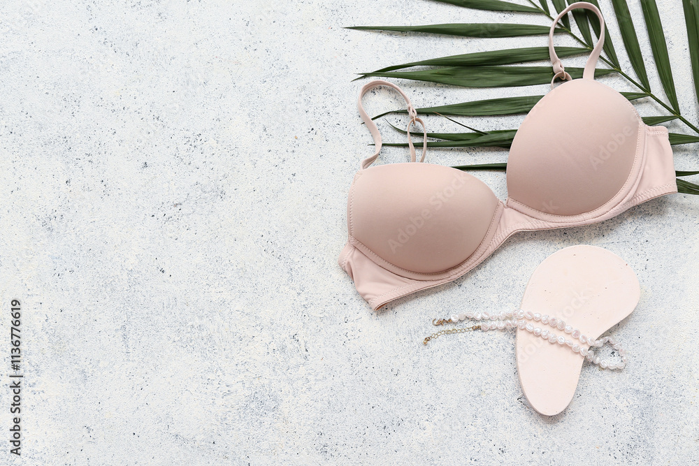 Stylish female bra, necklace and palm leaf on light background