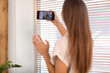 © Pixel-Shot - Young woman video chatting with family on mobile phone at home, back view