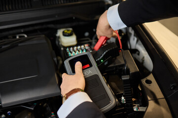 Closeup photo of black car battery connected with jumper cables for repair or recharging