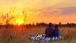 © Riko - Couple sitting on a blanket in a field during sunset with glowing horizon. Romantic nature and outdoor picnic concept