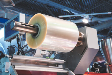 Poster - A roll of plastic film above a packaging conveyor for food packaging or plastic packaging bag production. The polyethylene film is fed from the roll into the machine