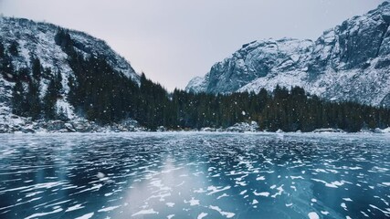 Wall Mural - aerial view from low flying drone of frozen lake in snowfall. mountains in winter at sunset. lofoten