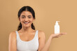 © Prostock-studio - A young Eastern Indian woman is smiling while holding a white bottle of skin care product. She is enjoying a pampering moment in a serene, isolated setting.