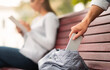 © Prostock-studio - Pickpocket Thief Stealing Mobile Phone From Woman's Bag While She Sitting On Bench In Park. Cropped, Selective Focus