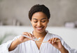 © Prostock-studio - African American woman happily brushes her teeth in a stylish bathroom, wearing a soft robe. She holds a bamboo toothbrush and applies toothpaste, showcasing her morning routine with joy.