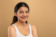 © Prostock-studio - A young Indian woman smiles while indulging in her skincare routine, surrounded by a warm, neutral backdrop. This moment showcases self-care and beauty practices among Gen Z, copy space