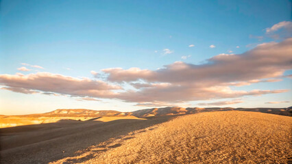 Wall Mural - Sunset over the desert landscape with mountains and clouds, creating a beautiful orange and yellow sky at dusk