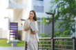 © amnaj - Young asian businesswoman holding a laptop while walking through a city park, gazing thoughtfully into the distance