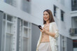 © amnaj - Asian businesswoman using smartphone in urban city smiling and holding mobile phone looking away