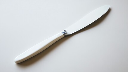 A white butter knife lies on a white surface.