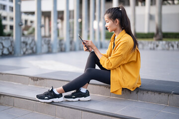 Wall Mural - Smiling young Asian woman using digital tablet in urban city