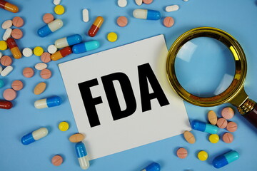 FDA - Food and Drug Administration text on sticky note paper with Medicine and Maginfying glass on blue background