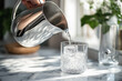 © kazakova0684 - A hand pouring water from a sleek silver pitcher into a frosty glass on a marble countertop