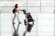 © Westend61 - Happy woman carrying baby daughter and pushing luggage cart at airport