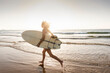 © Westend61 - Young woman running on beach, carrying surfboards