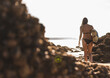 © Westend61 - France, Brittany, young woman carrying surfboard on a rocky beach at the sea