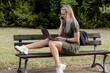 © MarijaBazarova - Serious blond businesswoman in black blazer sitting on bench in summer park using, typing on laptop computer and talking on the phone, studying outdoors. Female person working remote.