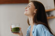 © SHOTPRIME STUDIO - Young woman enjoying a green smoothie in a cozy kitchen, representing healthy lifestyle and wellness, with a serene expression and natural light