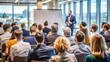 © engincan - Rear view of a diverse audience engaged in listening to a speaker delivering a presentation at a business conference hall