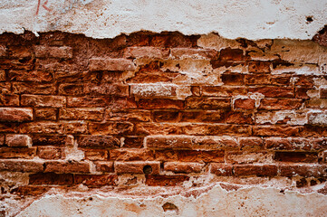 Brick wall with pieces of plaster. Wall of an old building in need of renovation. Aged wall texture of brick building close up. Grunge background with red and white blocks and layers of cement stucco