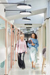 © Seventyfour - Vertical shot of smiling mature businesswoman walking along hallway of office center with female colleague cheerfully discussing work project in modern coworking space